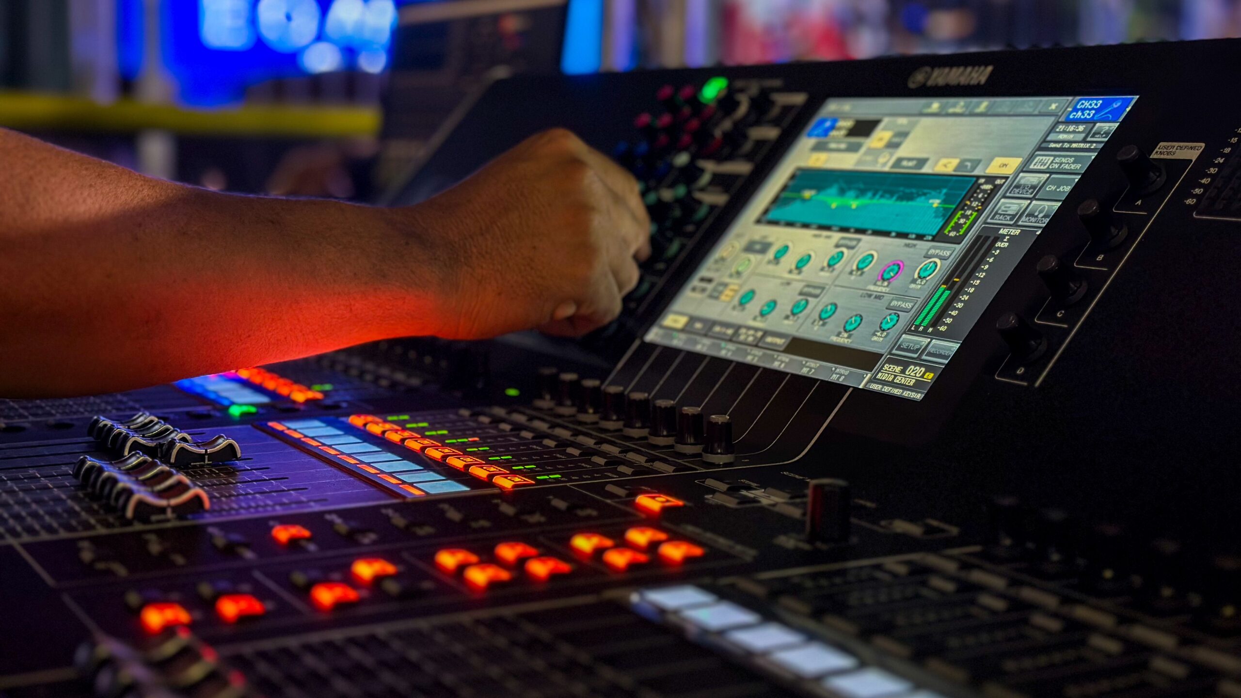 Operator's hand on a digital mixing console with a bright control screen