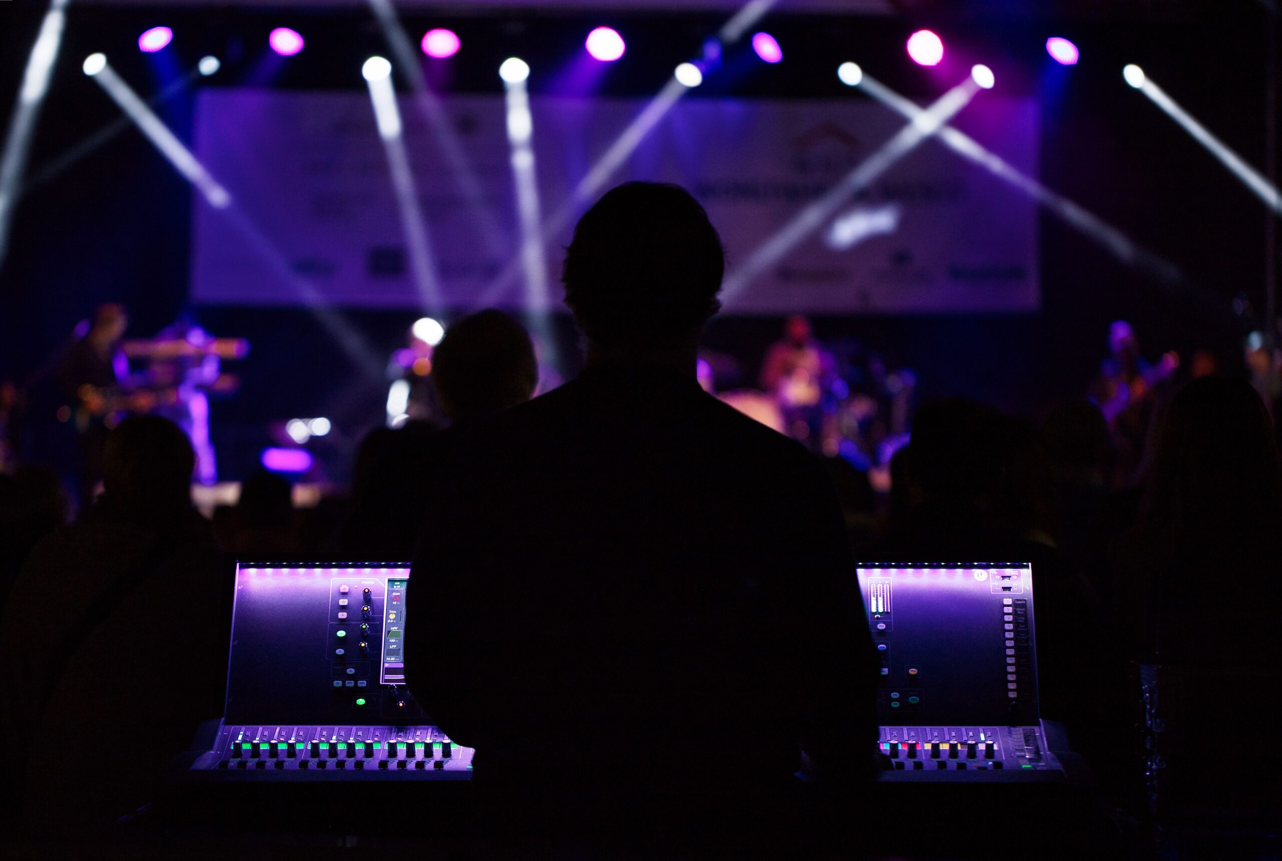 Live concert stage with overhead lighting truss and an audio operator at the mixing console